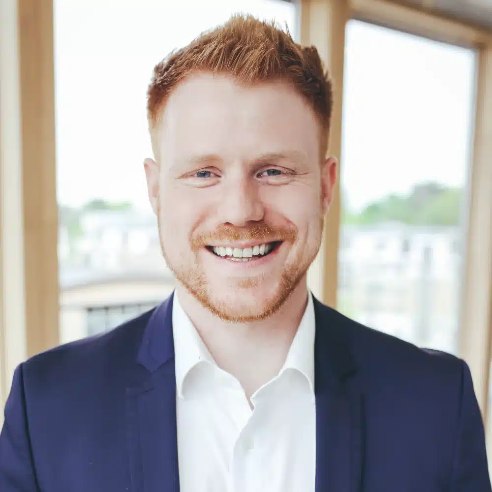 Shane_Gaynor Smiling man in suit with ginger hair indoors.